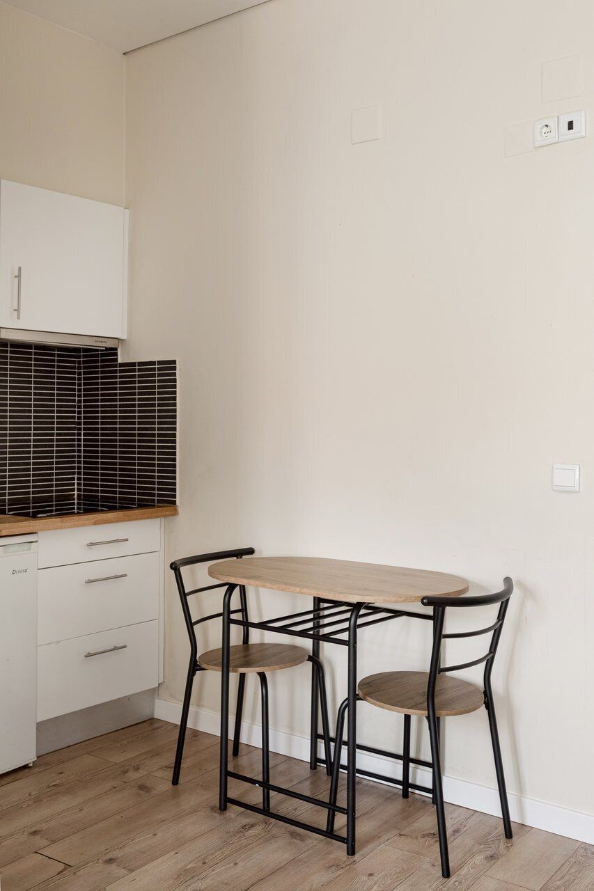 A kitchen with a wooden table and two chairs, a white cabinet, and a black tiled backsplash.
