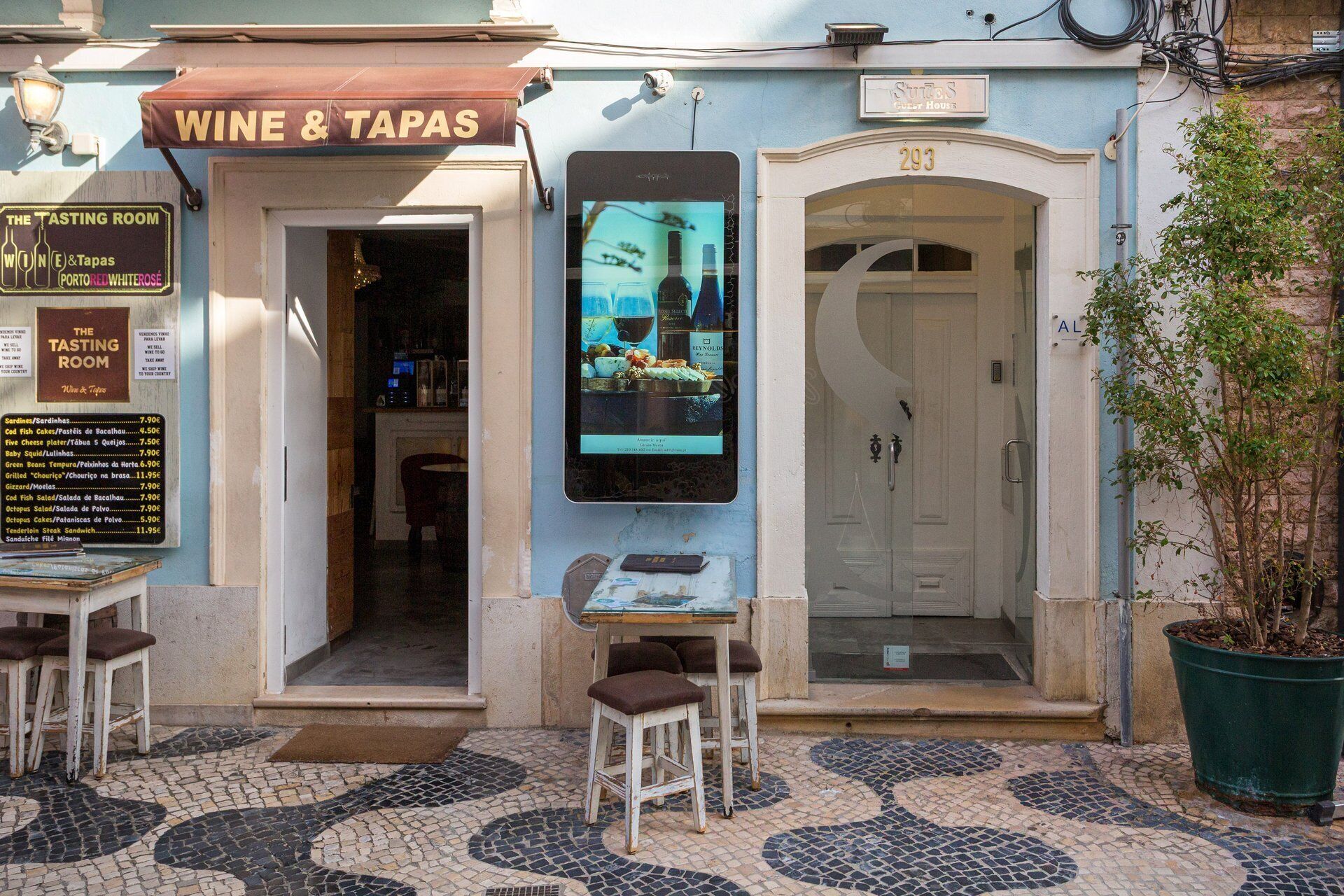 A restaurant named 'Wine & Tapas' with a menu board, outdoor seating, and a guest house entrance.