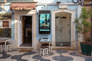En restaurant kaldet 'Wine & Tapas' med et menuskilt, udendørs siddepladser og indgang til et gæstehus.