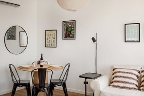 A dining area with a round table, chairs, a wine bottle, glasses, and framed botanical prints on the wall. - Seaside Family Stays | Walk to the Beach, Caxias (Caxias)