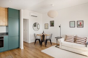 A modern kitchen with teal cabinets, a dining area with a round table and chairs, and a white sofa with striped pillows. - Seaside Family Stays | Walk to the Beach, Caxias (Caxias)
