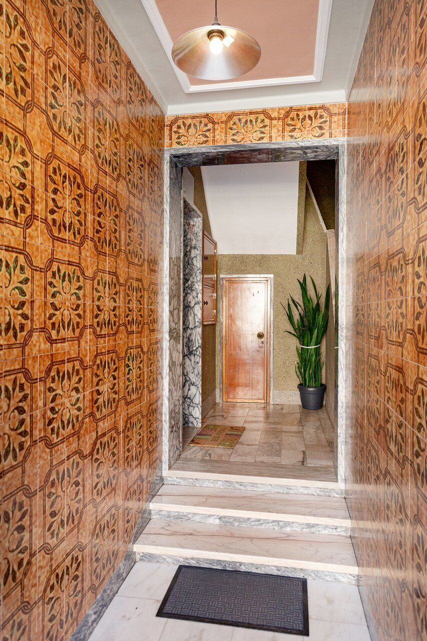 A hallway with patterned walls, a marble floor, a door, and a potted plant.