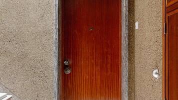 A wooden door with a metal handle, a marble threshold, and a smiley face mat on the floor.