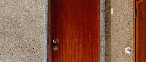 Una puerta de madera con un picaporte metálico, un umbral de mármol y un felpudo con una carita sonriente en el suelo.