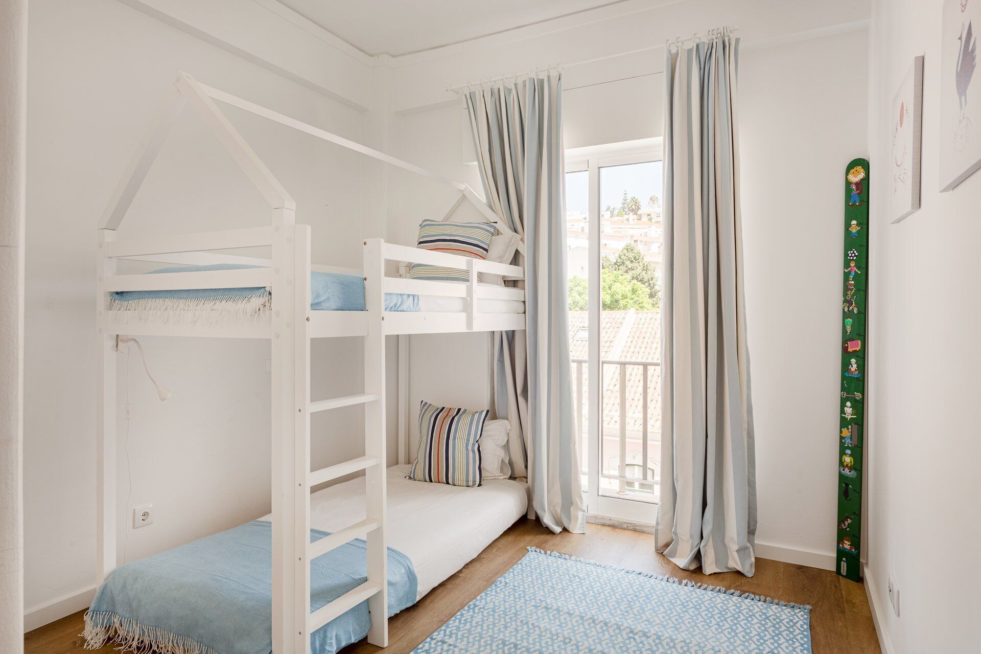 A bunk bed room with a window, curtains, and a green wall decoration.