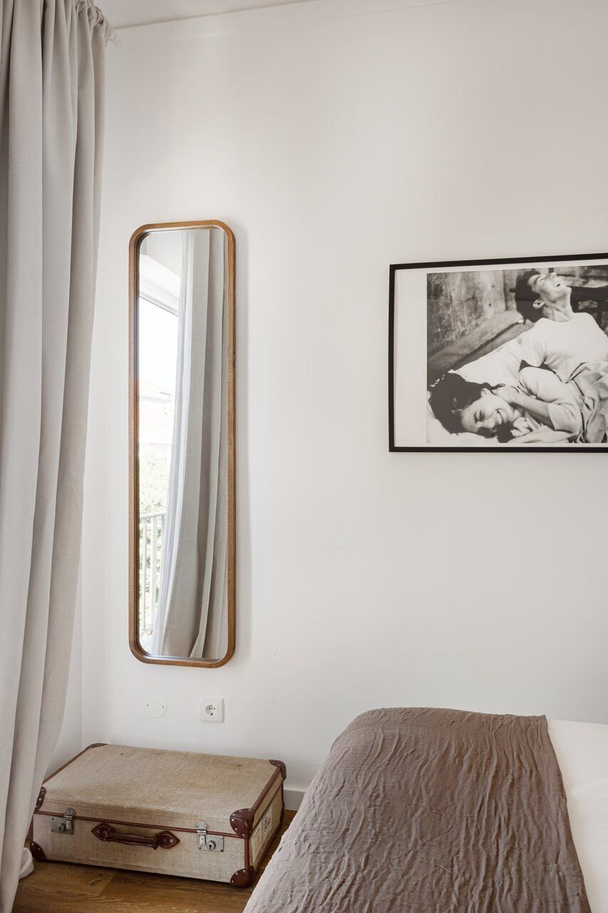 A room with a bed, a suitcase, a mirror, and a framed picture on the wall.