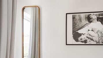 A room with a bed, a suitcase, a mirror, and a framed picture on the wall.