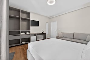 A bedroom with a bed, a grey sofa, a TV, a wardrobe, and a small desk with a kettle. - Casa Del Sol SeaSide (Durrës)