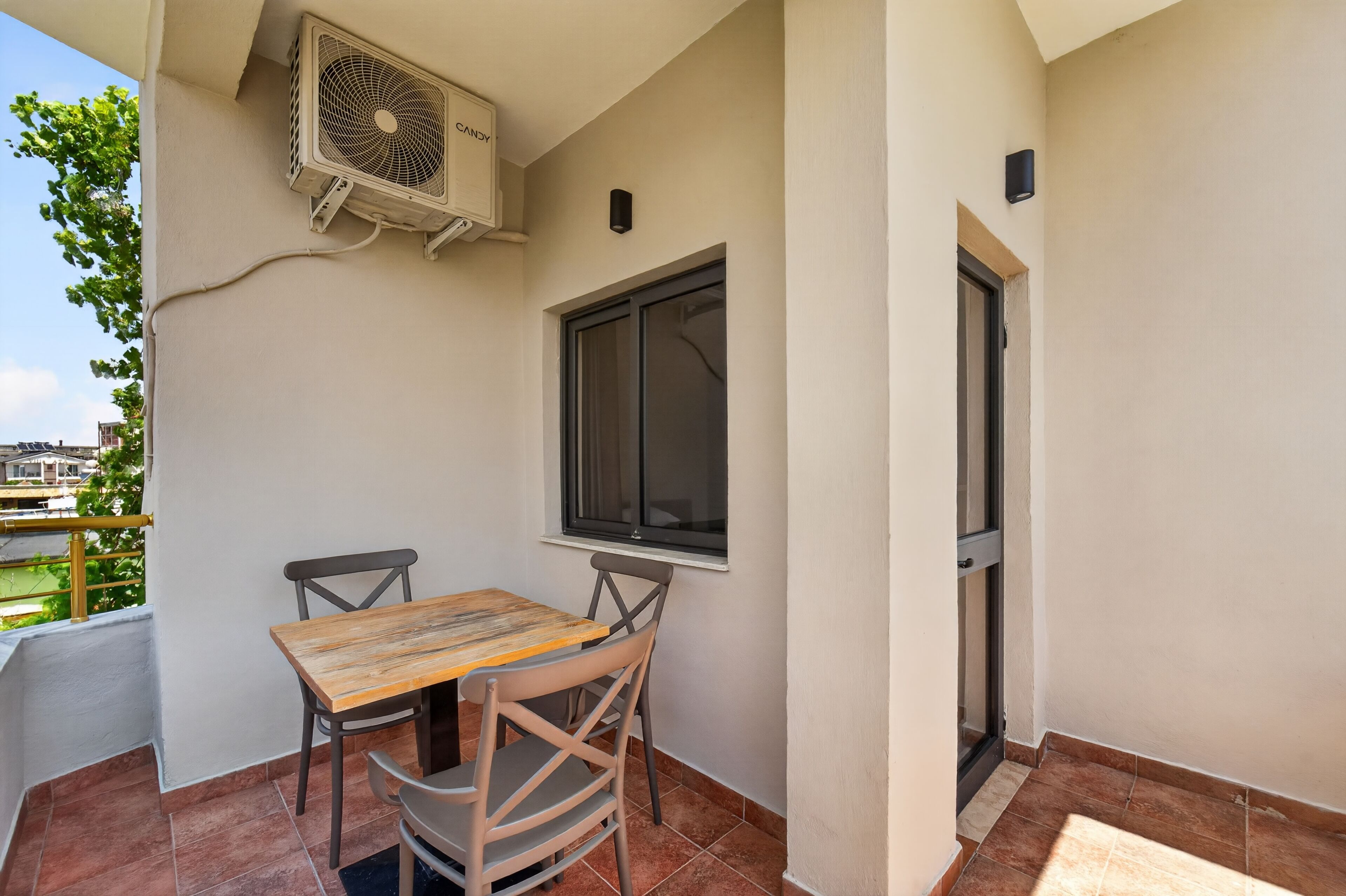 A balcony with a table and chairs, an air conditioning unit, a window, and a door.