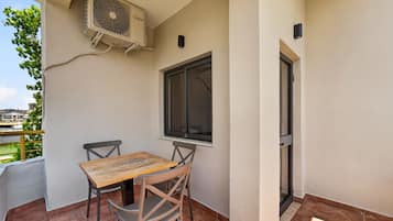 A balcony with a table and chairs, an air conditioning unit, a window, and a door.