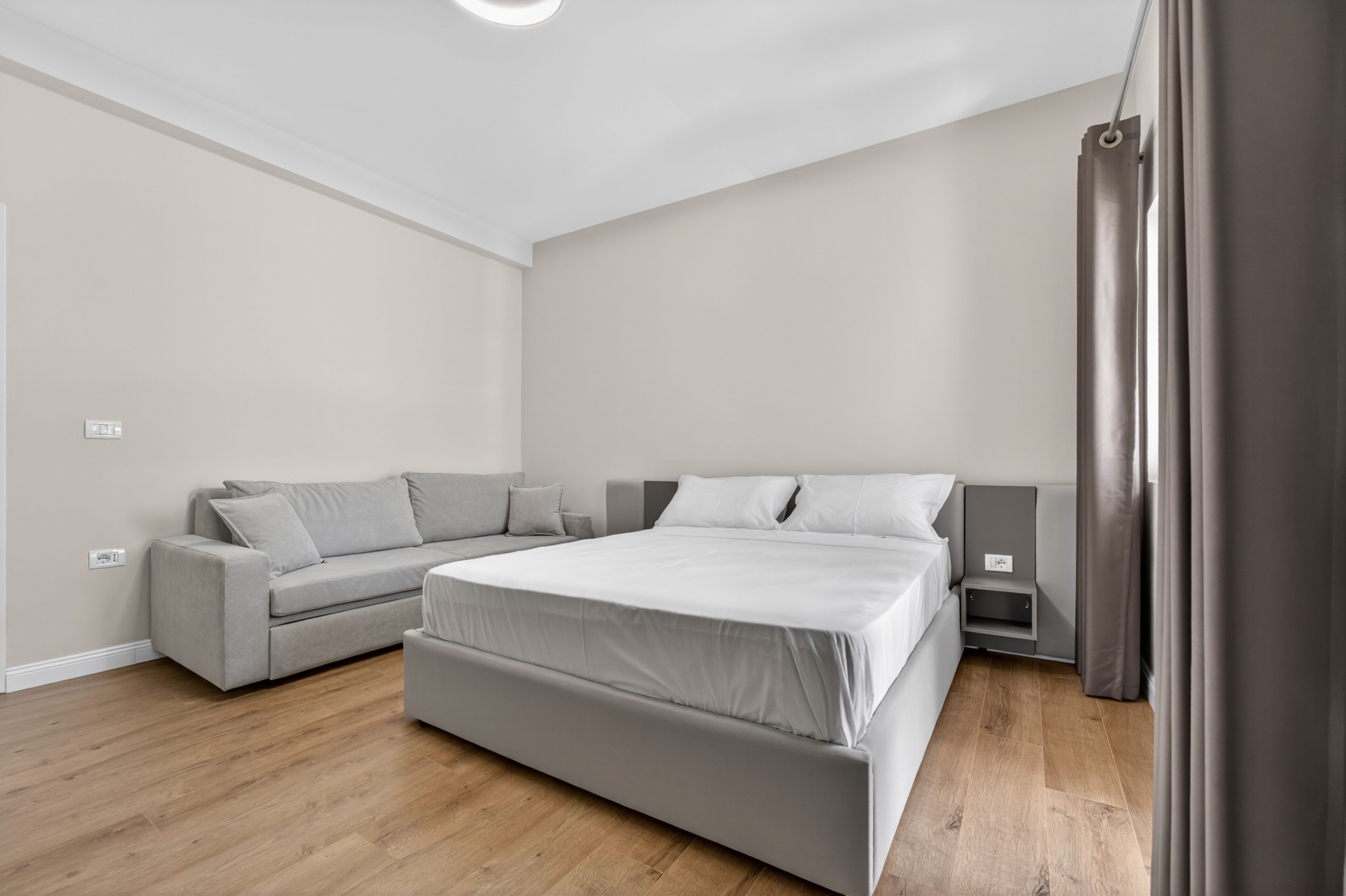 A modern bedroom with a bed, a sofa, a nightstand, and a curtain.