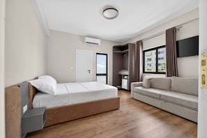 Ein modernes Hotelzimmer mit Bett, Sofa, Fernseher und einem Fenster mit Vorhängen.