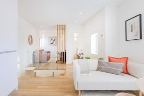 Ein modernes Wohnzimmer mit einem weißen Sofa, einer Glastrennwand und Holzboden.