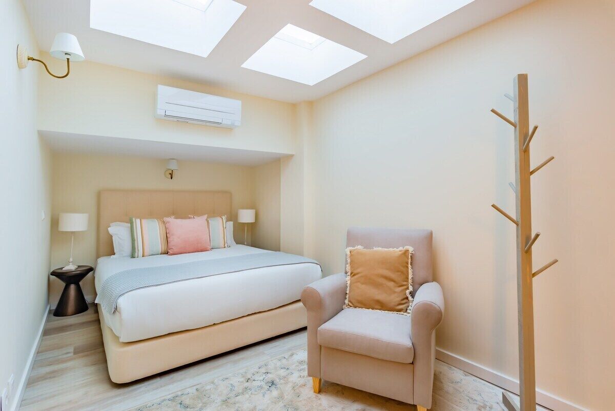 Une chambre à coucher comprenant un lit, une chaise, une table de chevet, un appareil de climatisation et des fenêtres de toit.