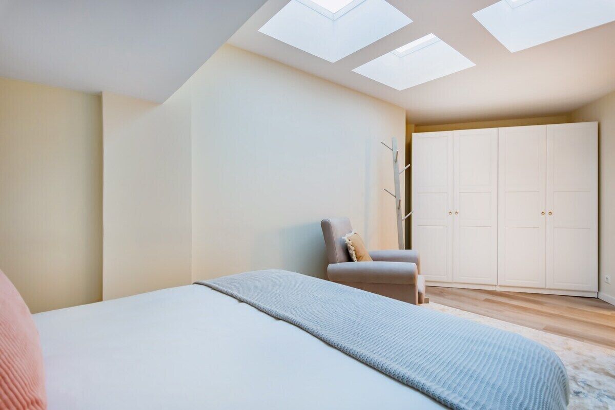 A bedroom with a bed, a chair, a wardrobe, and skylights.