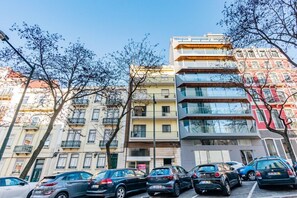 Ein mehrstöckiges Gebäude mit Balkonen, parkenden Autos und Bäumen.