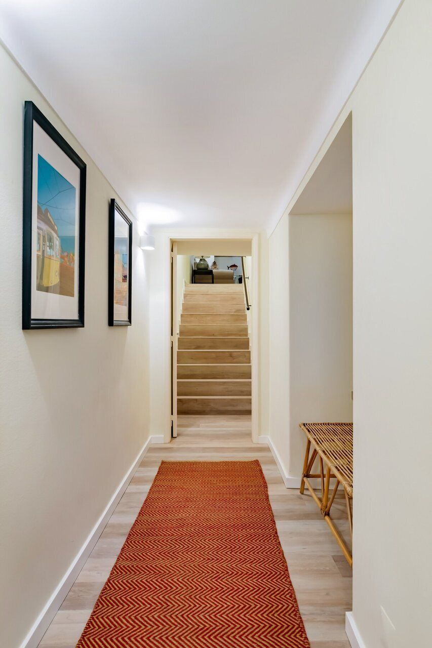 A hallway with a wooden staircase, a patterned rug, and framed pictures on the wall.