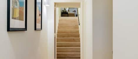 Un pasillo con una escalera de madera, un tapete estampado y cuadros en la pared.