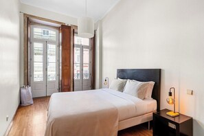 Ein Schlafzimmer mit Bett, Nachttisch, Lampe und Blick durch eine Tür.