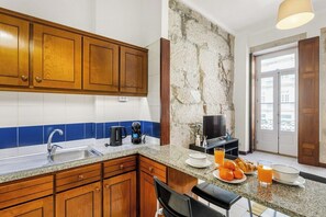 Eine Küche mit Holzschränken, einer Granit Arbeitsplatte, einem Spülbecken, einer Kaffeemaschine, einem Fernseher und Frühstücksangeboten.