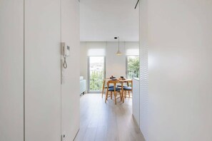 Ein Flur, der zu einem Essbereich mit Tisch und Stühlen sowie einer Pendelleuchte und einer weißen Wand mit Telefon führt.