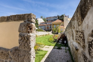 A courtyard with a stone wall, a grassy area, and buildings in the background. - Porto Garden | Patio Retreat (Porto)