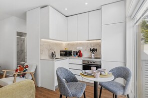 A compact kitchen with white cabinets, a built-in stove, and a dining area with two chairs. - Porto Garden | Patio Retreat (Porto)