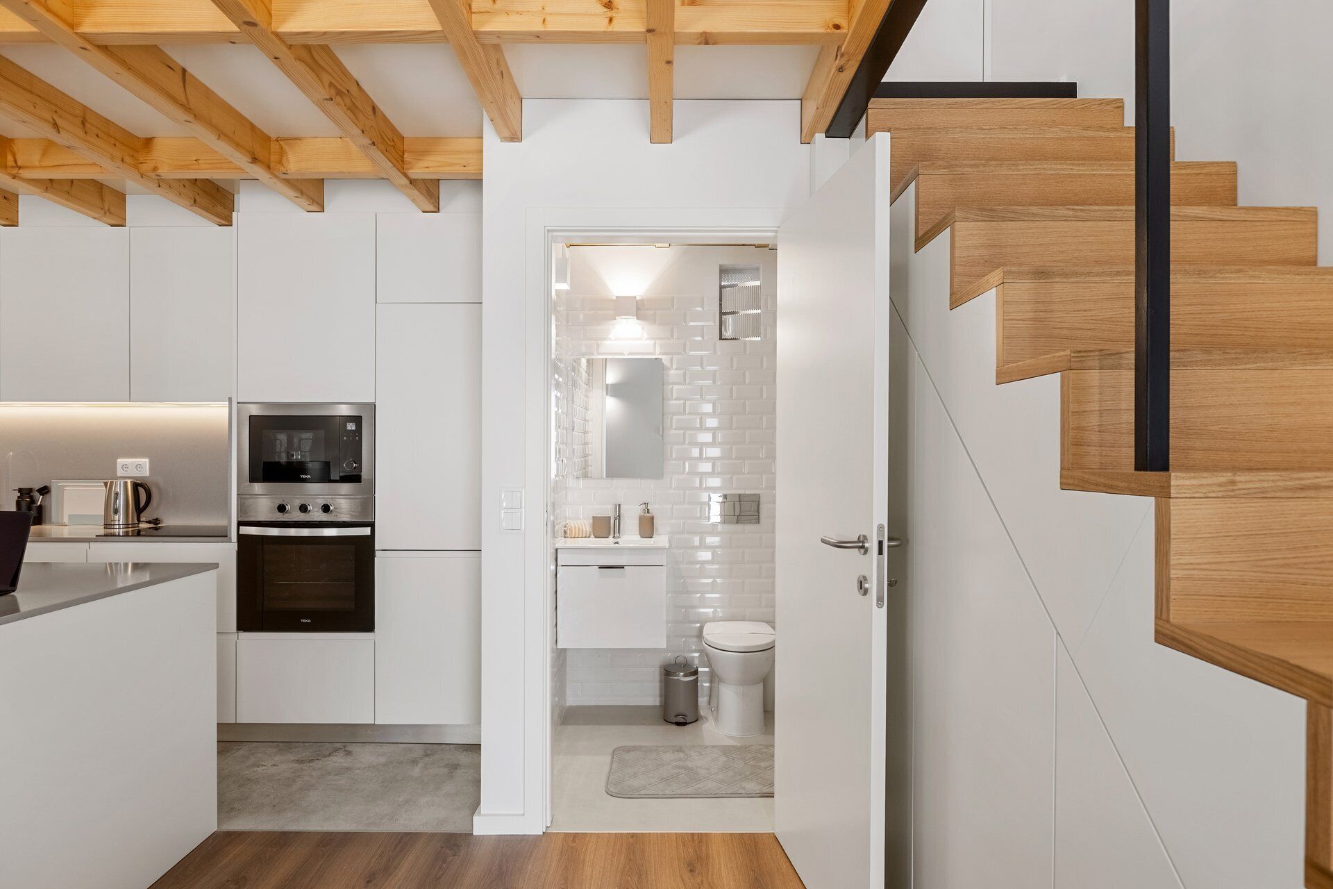 Une cuisine moderne dotée d’appareils électroménagers intégrés, d’un escalier en bois et d’une salle de bain au style minimaliste.