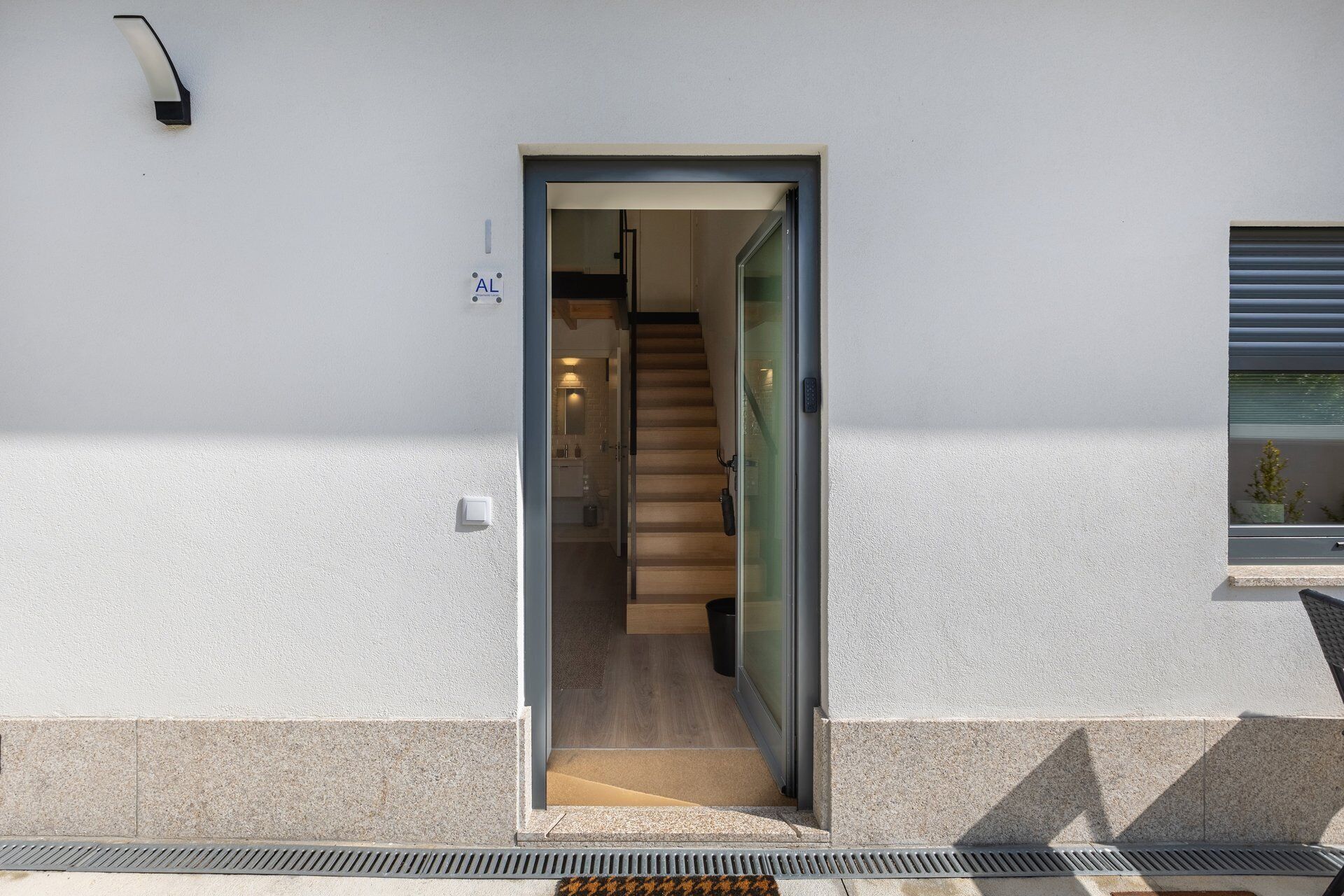 Une entrée moderne avec une porte en verre, un escalier apparent et un petit espace extérieur agrémenté d’une plante en pot.