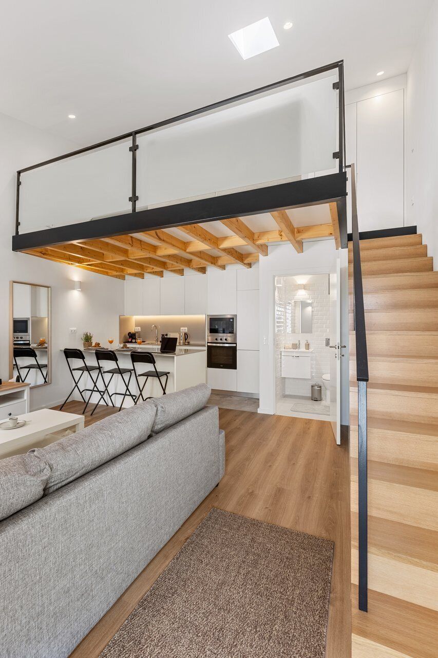 A modern interior with a loft-style staircase, a kitchen area, and a seating area with a sofa and chairs.