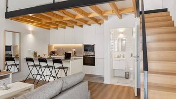 Un intérieur moderne avec un escalier de style industriel, un coin cuisine et un espace salon comprenant un canapé et des fauteuils.