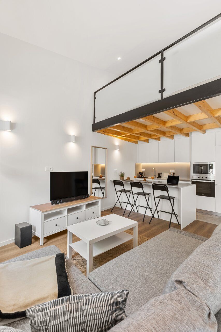 Un salon moderne doté d’un téléviseur à écran plat, de meubles blancs, d’un canapé et d’un coin cuisine avec une table à manger.