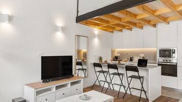 Un salon moderne doté d’un téléviseur à écran plat, de meubles blancs, d’un canapé et d’un coin cuisine avec une table à manger.