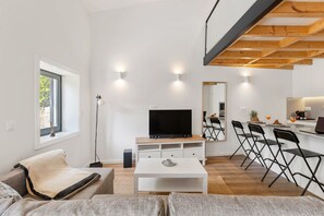 A modern living room with a flat-screen TV, a dining area with chairs, and a kitchen visible in the reflection. - Oliveira do Douro Studio (Vila Nova de Gaia)