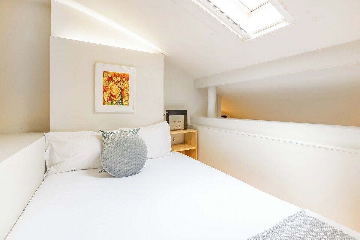 Ein Schlafzimmer mit Bett, Nachttisch, kleiner Ablagefläche und einem gerahmten Bild an der Wand.