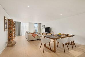 Ett modernt vardagsrum med en soffa, ett matbord och stolar, en tv och utsikt över staden.