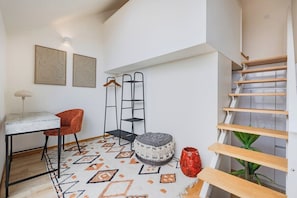 A modern interior with a staircase, a dining area with a table and chairs, and a patterned rug. - Saldanha Boho Duplex (Porto)