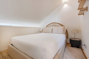 A bedroom with a bed, a bedside lamp, a wall-mounted shelf, and a window. - Saldanha Boho Duplex (Porto)