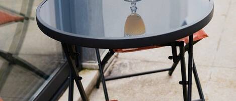 Een glazen tafel met een glas sinaasappelsap en een gestreept rietje, samen met twee oranje stoelen van mesh-materiaal.