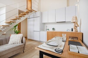 A modern kitchen with white cabinets, a wooden dining table set with plates and glasses, a staircase with wooden steps, and a plant. - Saldanha Boho Duplex (Porto)