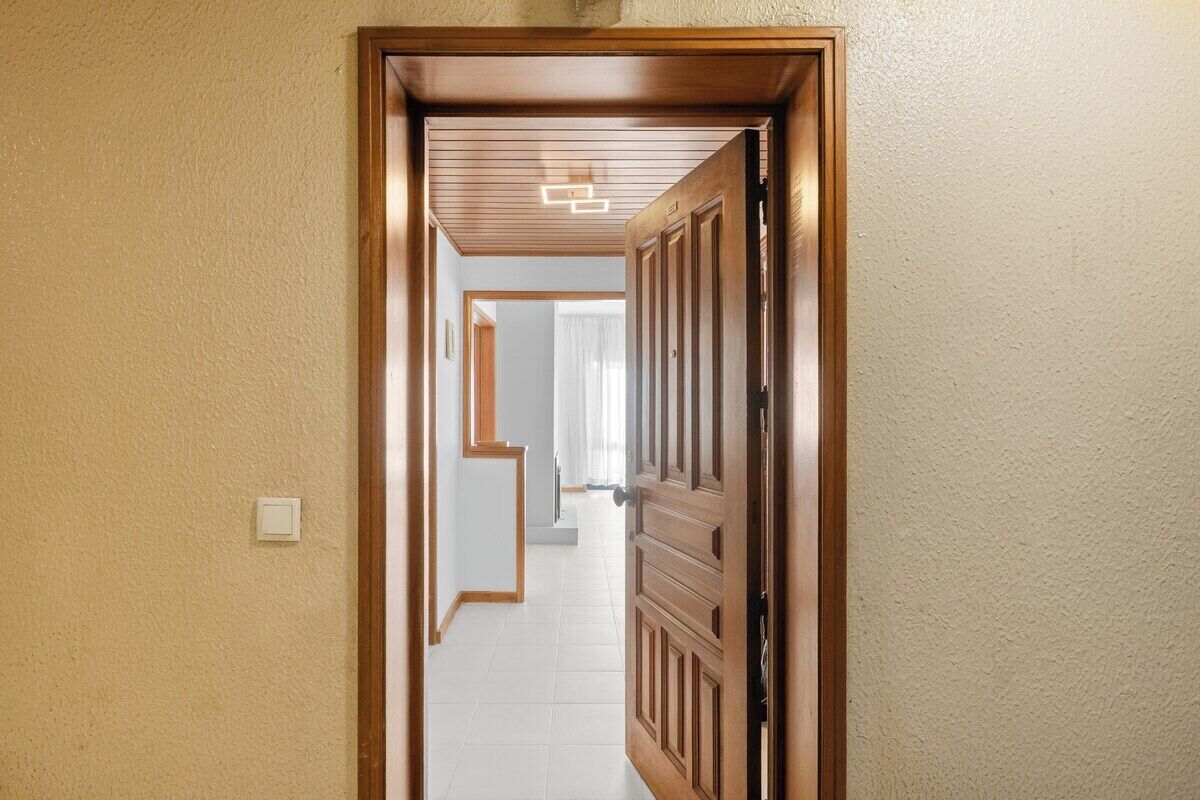 Ein Korridor mit einer Holztür, einem Lichtschalter und einer Deckenleuchte.