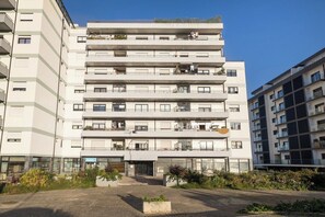Ein mehrstöckiges Wohngebäude mit Balkonen, einem zentralen Eingangsbereich und einem gepflasterten Innenhof.