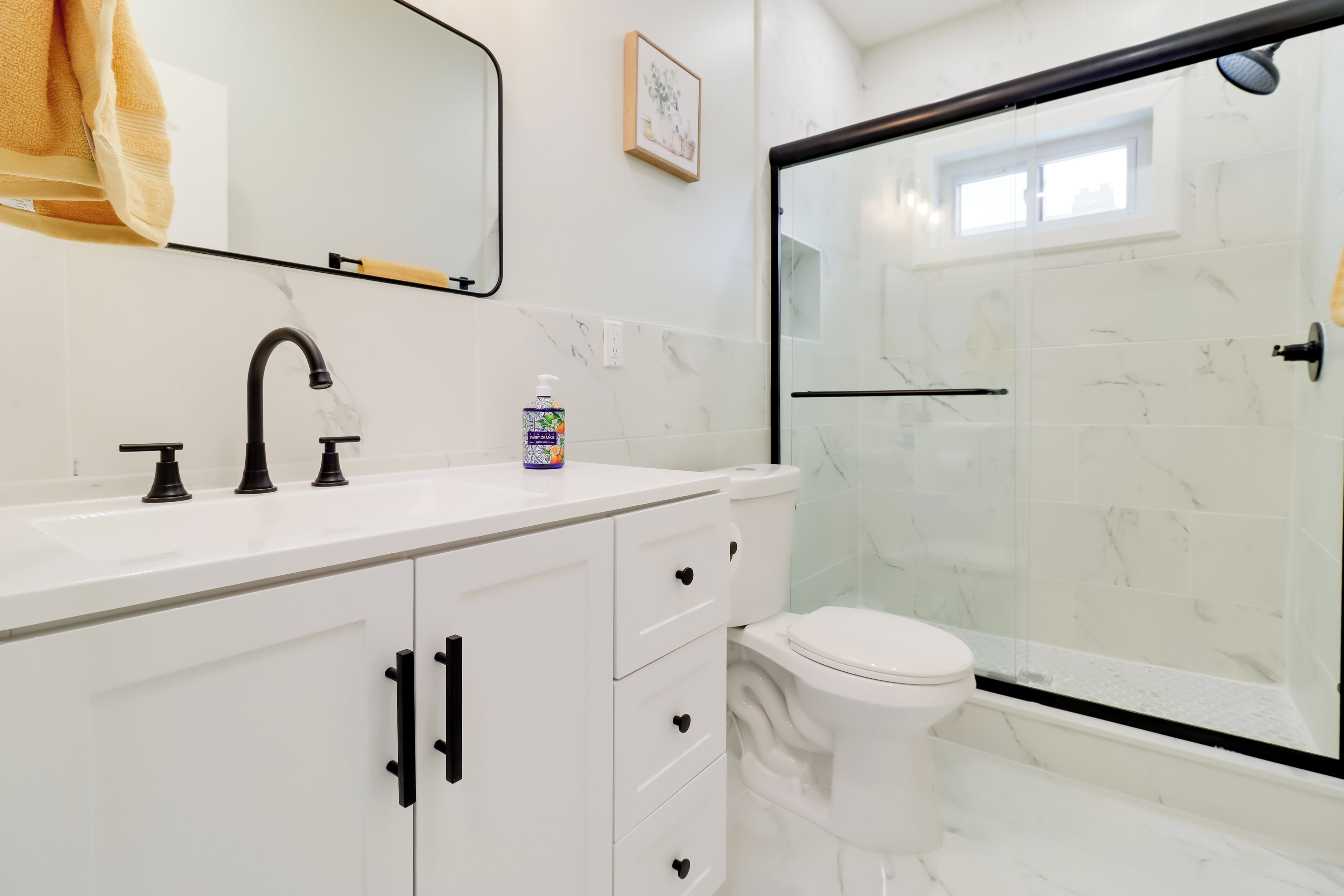 A bathroom with a white vanity, a black faucet, a toilet, and a glass shower enclosure.