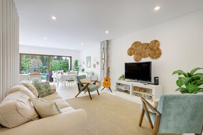 Ein modernes Wohnzimmer mit einer Couch, Sesseln, einem Fernseher und einer Gitarre.