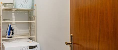 A compact laundry room with a front-loading washing machine, shelves with baskets, and a wooden door.