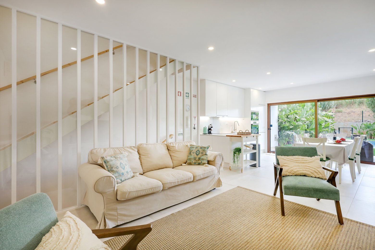 A modern living room with a sofa, a chair, a staircase, and a view of the outdoors.