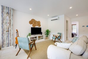 Ein Wohnzimmer mit Fernseher, Gitarre, Sofa und Sessel.