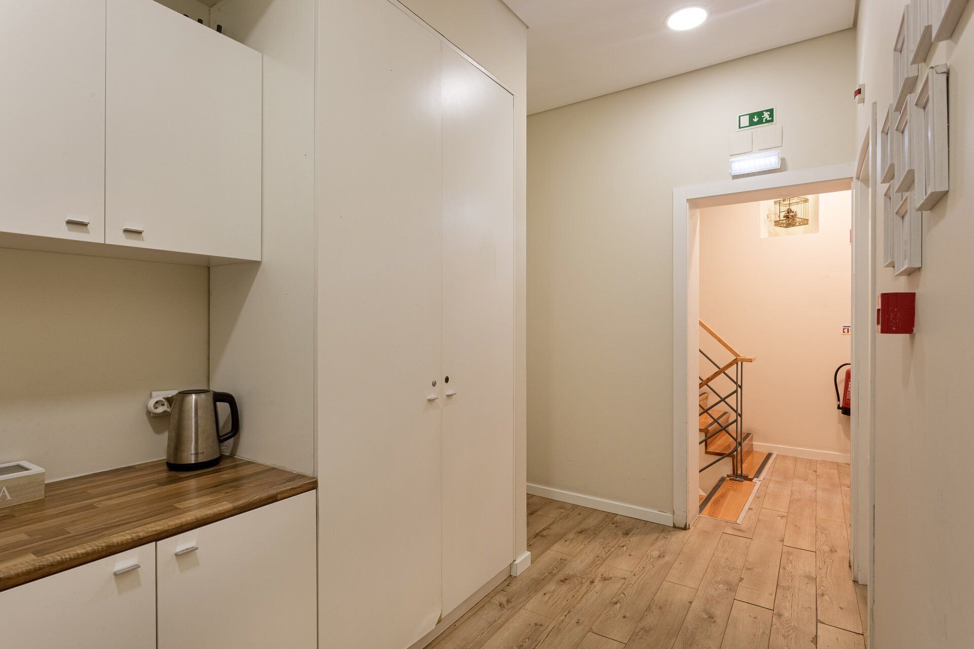 Un pasillo con suelo de madera, una kitchenette con hervidor y una escalera que lleva a otra habitación.