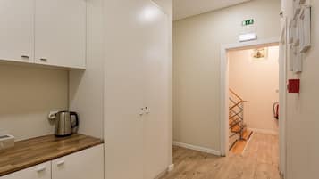 Un pasillo con suelo de madera, una kitchenette con hervidor y una escalera que lleva a otra habitación.