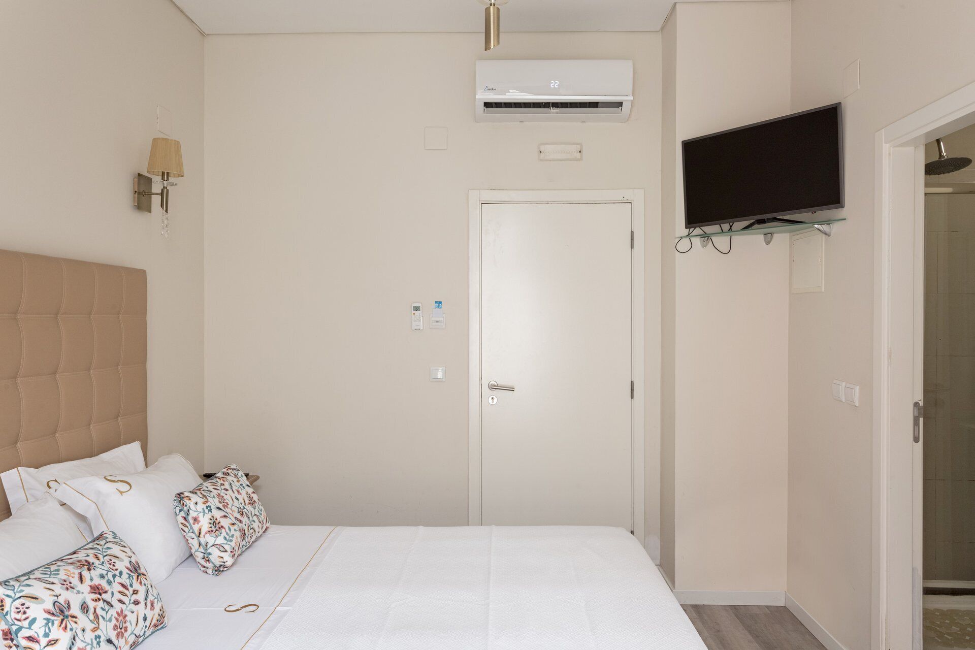 Ein Schlafzimmer mit einem Bett, einem an der Wand montierten Fernseher, einer Klimaanlage und einer Tür.
